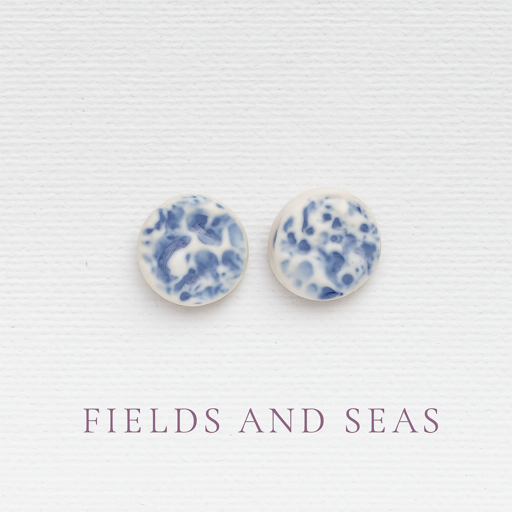 Porcelain sea pebble stud earrings on white canvas background with blue marbled glaze pattern.