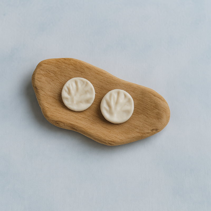 A pair of white porcelain coral-textured stud earrings displayed on a smooth piece of organic wood