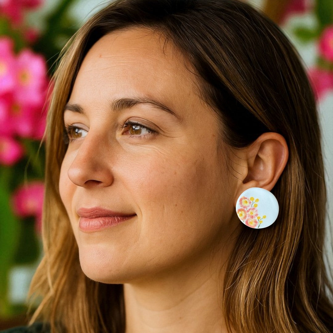 Porcelain stud earrings hand-painted with pink paper daisies and yellow billy buttons, displayed on model.