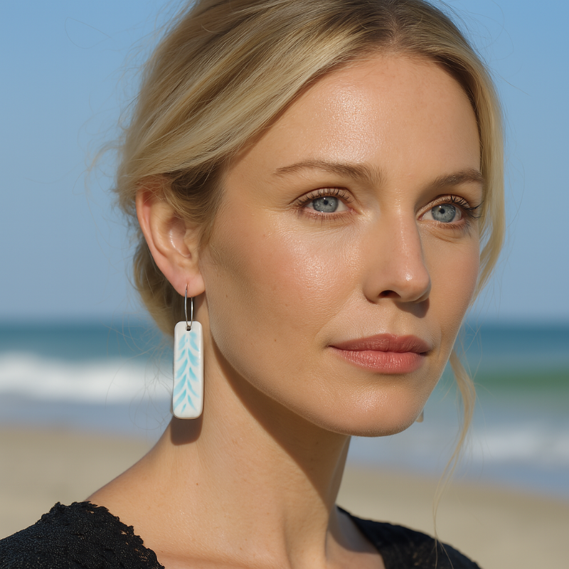 A pair of rectangular porcelain earrings in baby blue with sea leaf textures on a model with handmade sterling silver hooks.