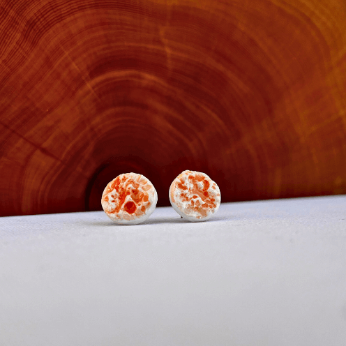 Porcelain sea pebble stud earrings on white canvas background with orange marbled glaze pattern.