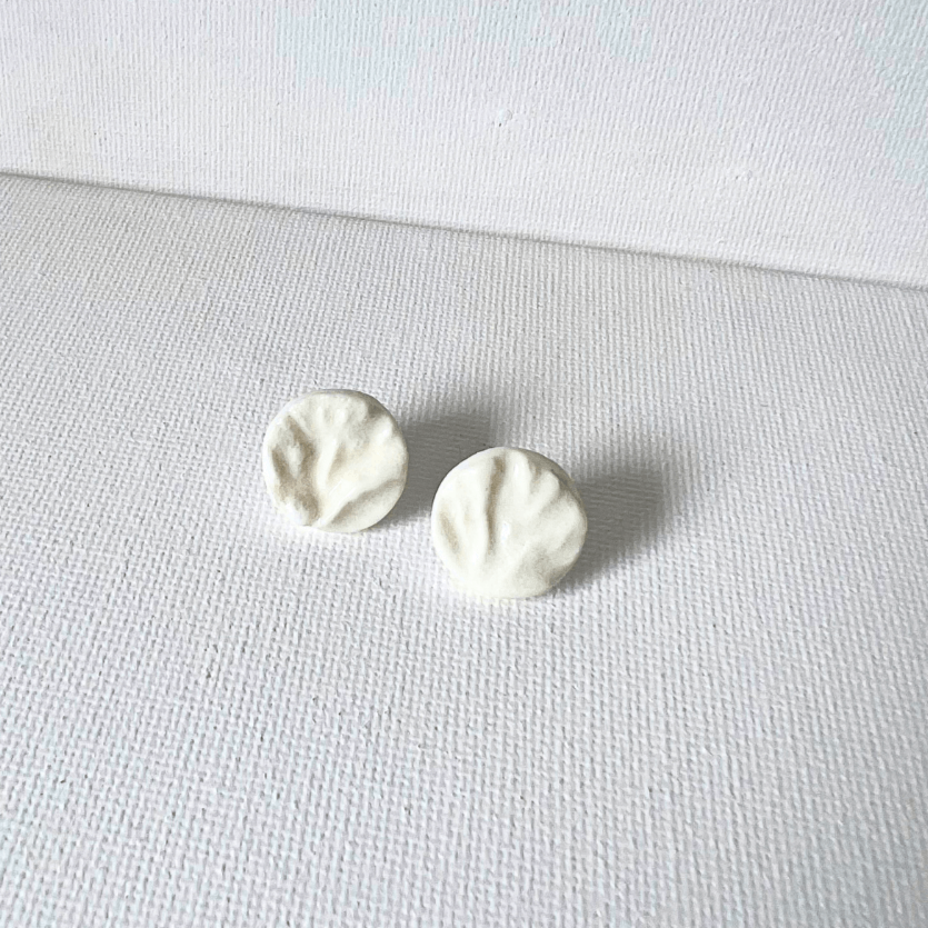 A pair of white porcelain coral-textured stud earrings displayed on a smooth piece of organic wood