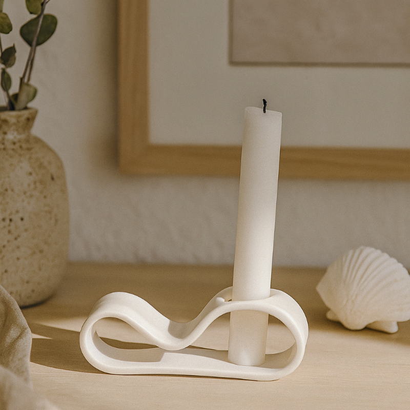 Sculptural white porcelain candle holder with taper candle, styled on a timber surface against a white background.