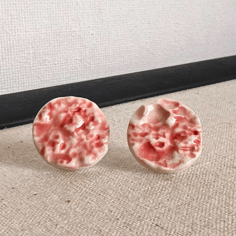 Porcelain sea pebble stud earrings on white canvas background with red marbled glaze pattern.