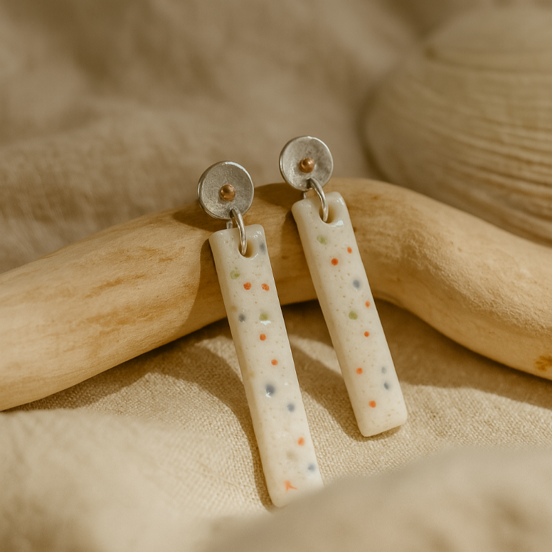 Pair of handmade porcelain earrings with subtle multicolour dots and sterling silver and copper beaten stud tops, photographed against linen