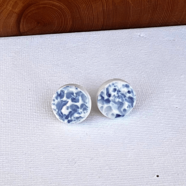 Porcelain sea pebble stud earrings on white canvas background with blue marbled glaze pattern.