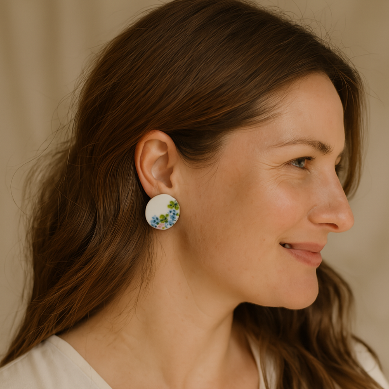 Round hand-painted porcelain earrings with pink, blue, and yellow floral designs on a model.