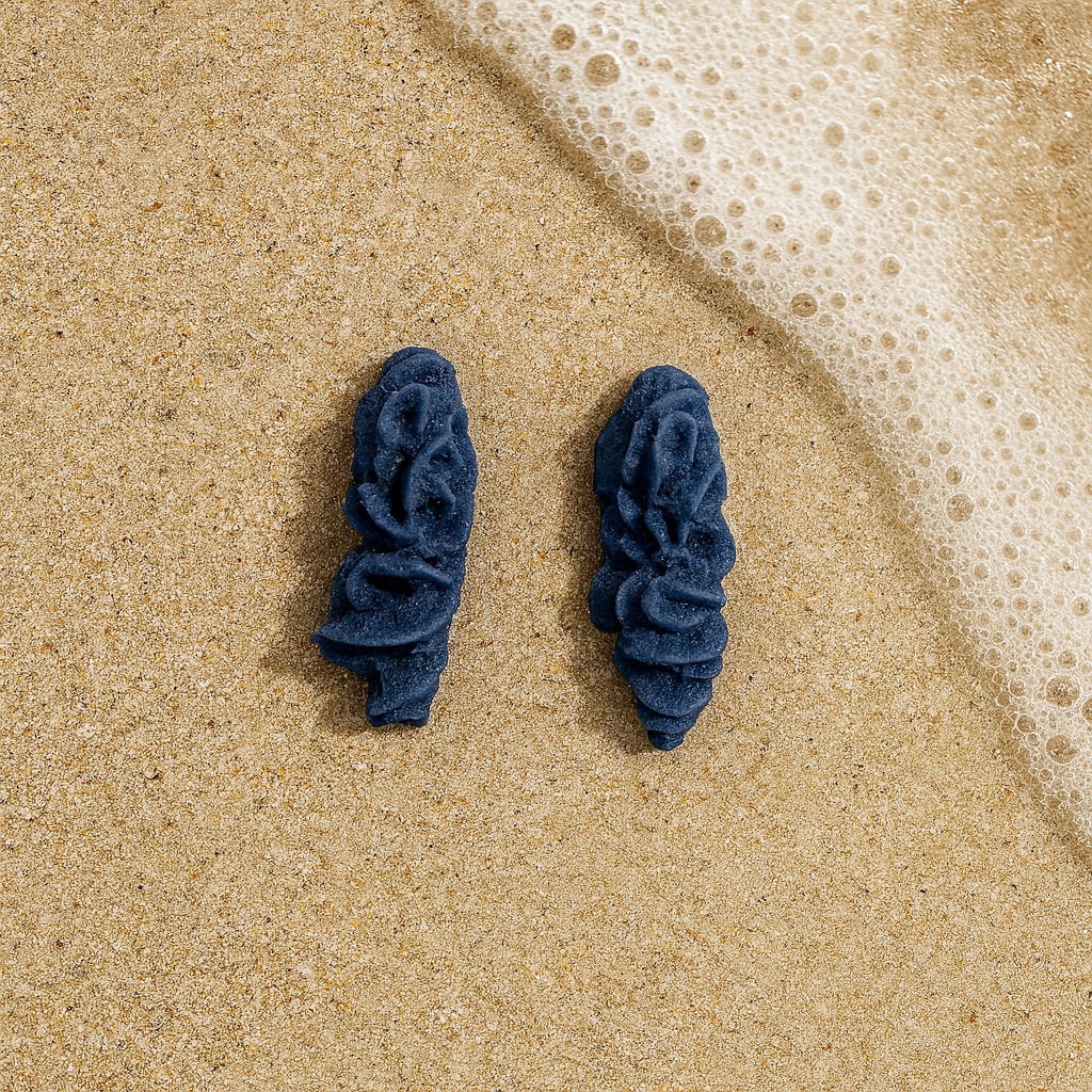 Pair of deep cobalt blue porcelain coral earrings on sand by the sea.