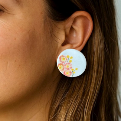 Porcelain stud earrings hand-painted with pink paper daisies and yellow billy buttons, displayed on a model.