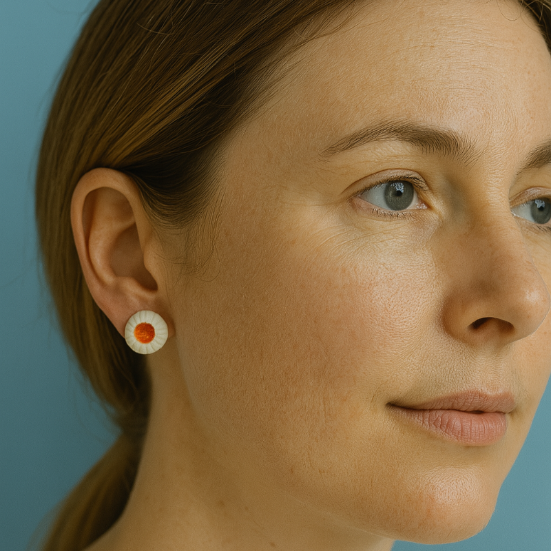 Pair of handmade porcelain earrings shaped like sea anemones, featuring white rippled edges and a bold orange center.