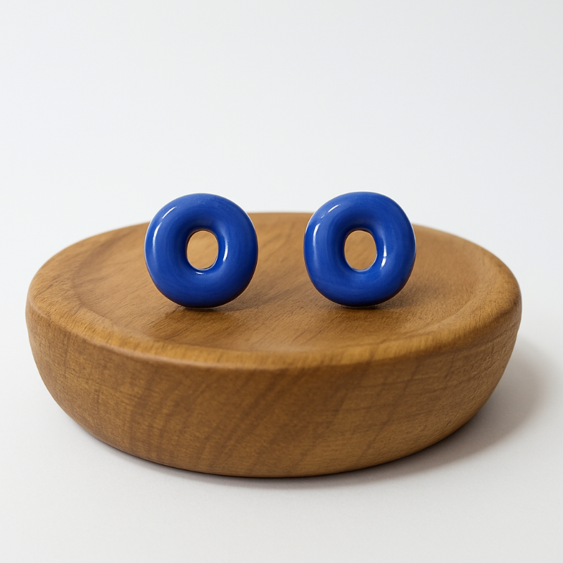 Blue donut-shaped earrings on a wooden stand with a white background