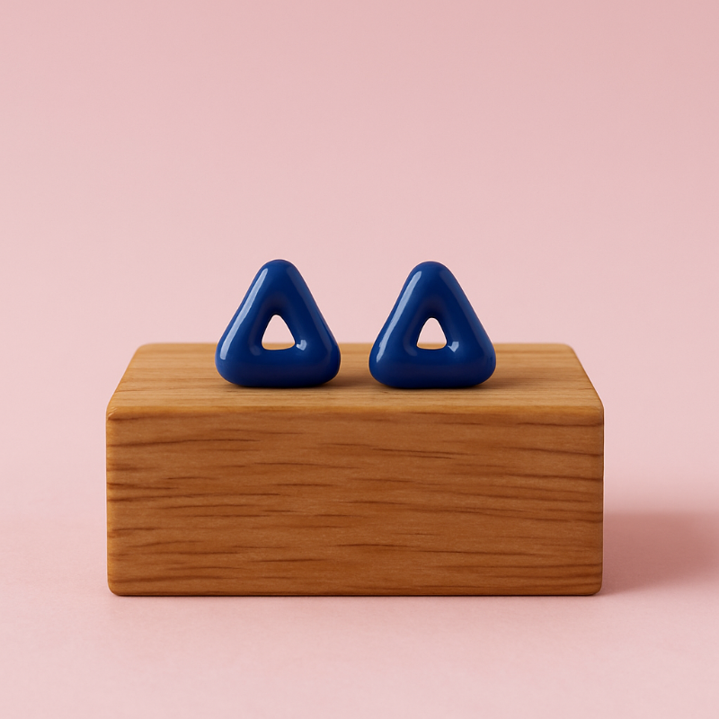 Blue triangular earrings on a wooden block against a pink background