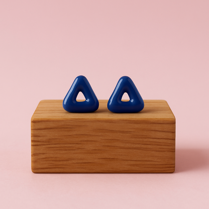 Blue triangular earrings on a wooden block against a pink background