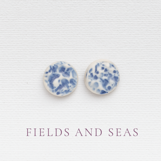 Porcelain sea pebble stud earrings on white canvas background with blue marbled glaze pattern.
