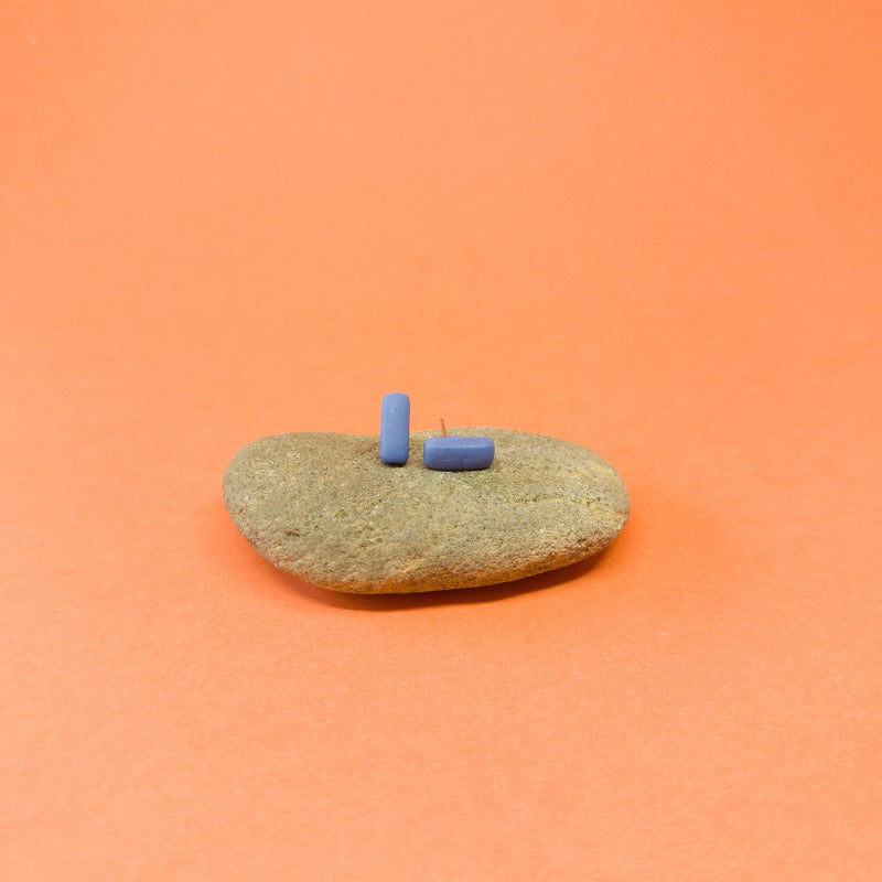 Blue porcelain bar stud earrings resting on a smooth stone