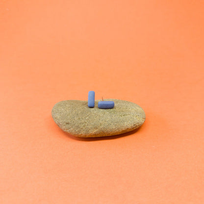 Blue porcelain bar stud earrings resting on a smooth stone