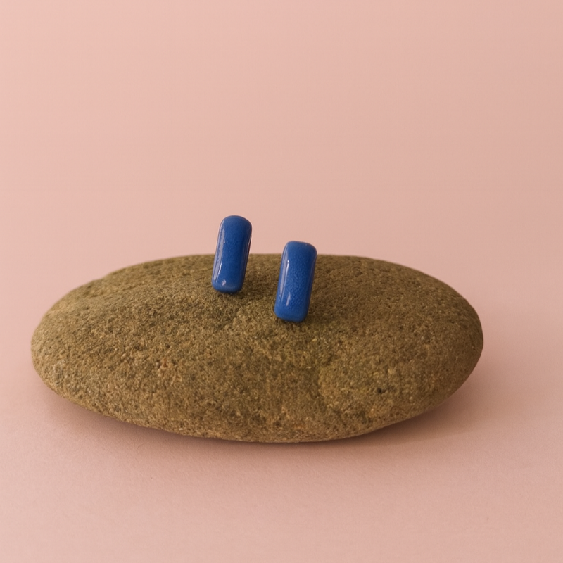 Blue porcelain bar stud earrings resting on a smooth stone