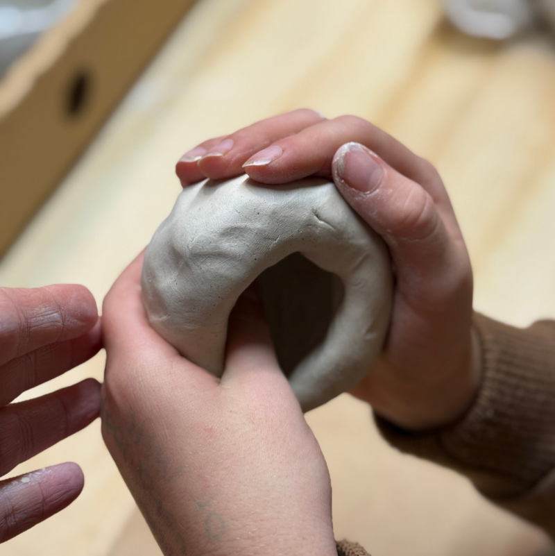 Hands shaping a clay pinch pot cup during a beginner-friendly pottery workshop.