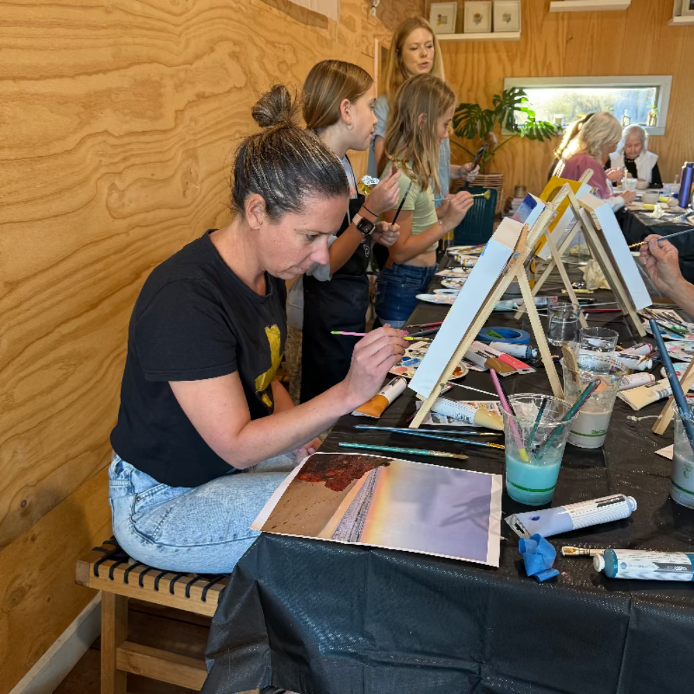 Group of people painting at a table in a studio setting