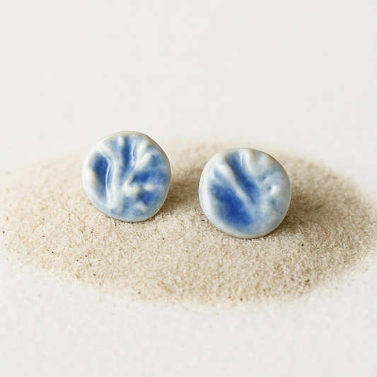 A pair of round porcelain stud earrings with coral-molded texture, blue wash, and clear glaze.