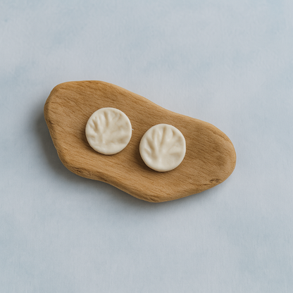A pair of white porcelain coral-textured stud earrings displayed on a smooth piece of organic wood