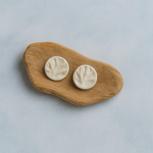 A pair of white porcelain coral-textured stud earrings displayed on a smooth piece of organic wood