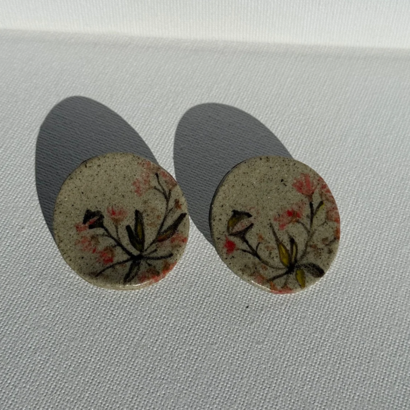 Pair of round handcrafted ceramic earrings painted with Australian gum leaves, blossoms, and gumnuts on speckled clay, 3.5 cm wide.