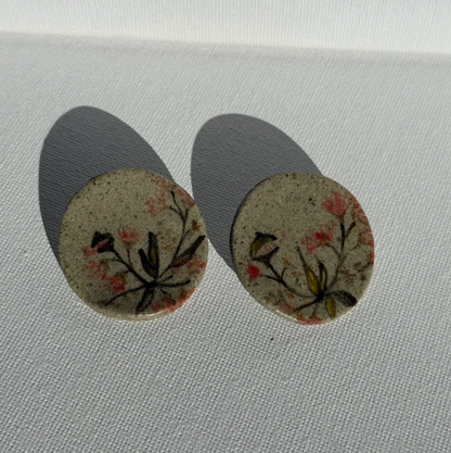 Pair of round handcrafted ceramic earrings painted with Australian gum leaves, blossoms, and gumnuts on speckled clay, 3.5 cm wide.