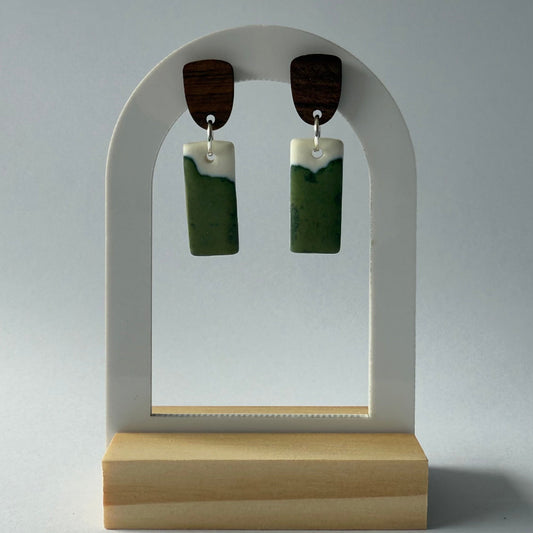 Close-up of handmade porcelain dangle earrings featuring organic green glaze and wooden studs, inspired by coastal inlets.