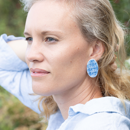 Close-up of woman wearing oval cobalt blue porcelain statement earrings with organic wave texture, inspired by ocean tide lines.