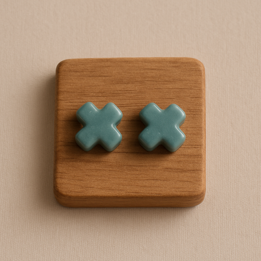 Pair of small porcelain cross stud earrings in soft green Laguna clay on neutral background