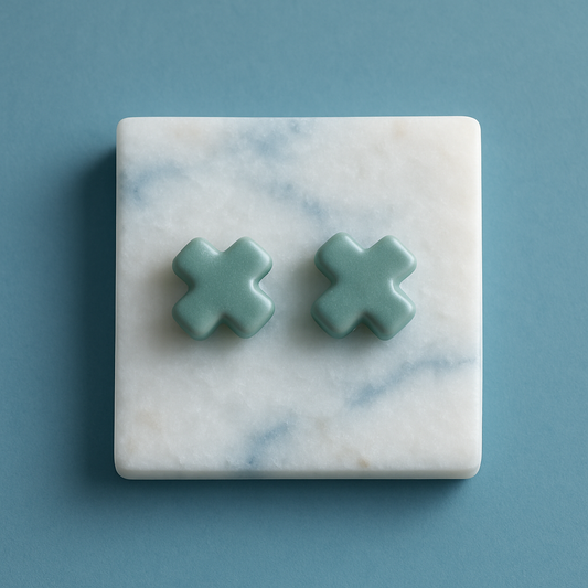 Pair of small porcelain cross stud earrings in soft green Laguna clay on neutral background