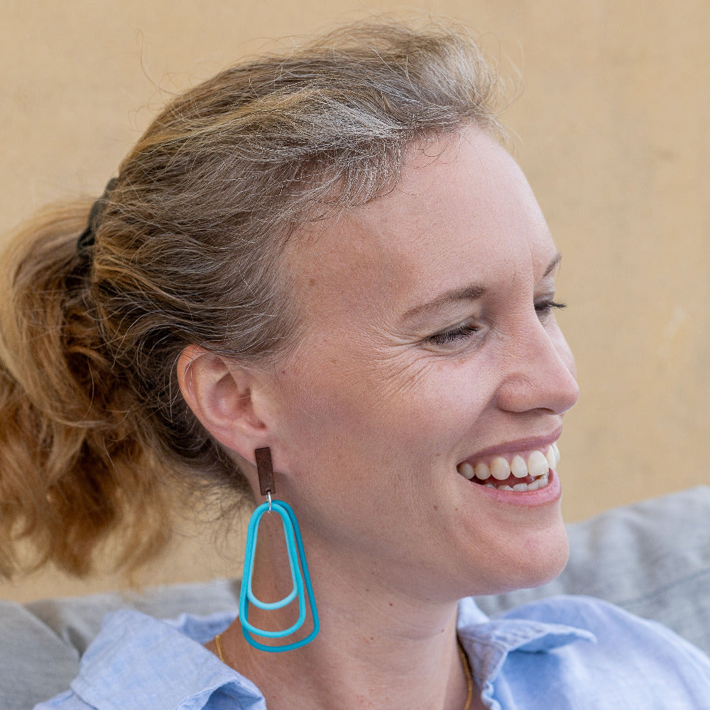 Woman wearing monochromatic teal dangle earrings. Light and easy wearing. 