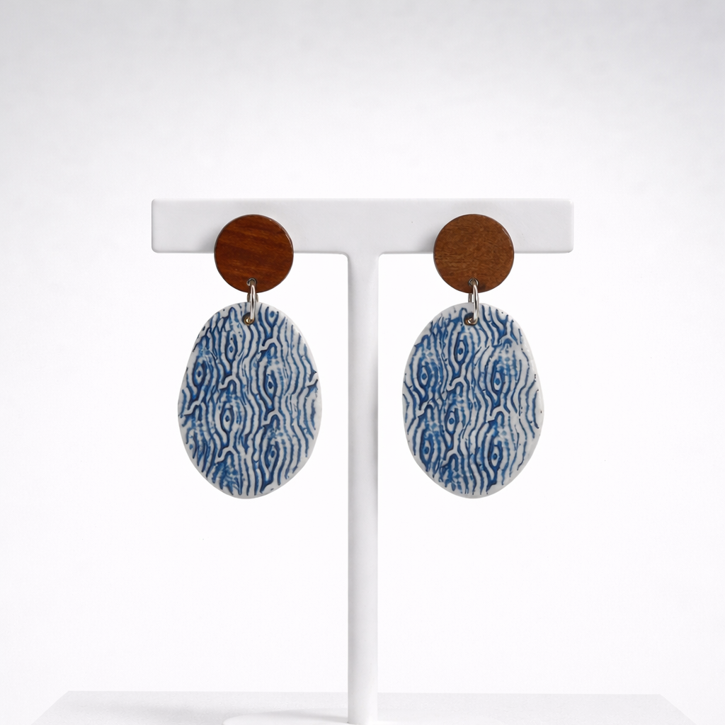 Handmade oval porcelain dangle earrings with blue and white sea-inspired pattern and wooden studs on a white background