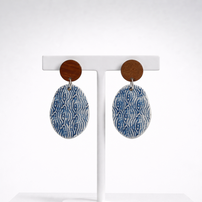 Handmade oval porcelain dangle earrings with blue and white sea-inspired pattern and wooden studs on a white background