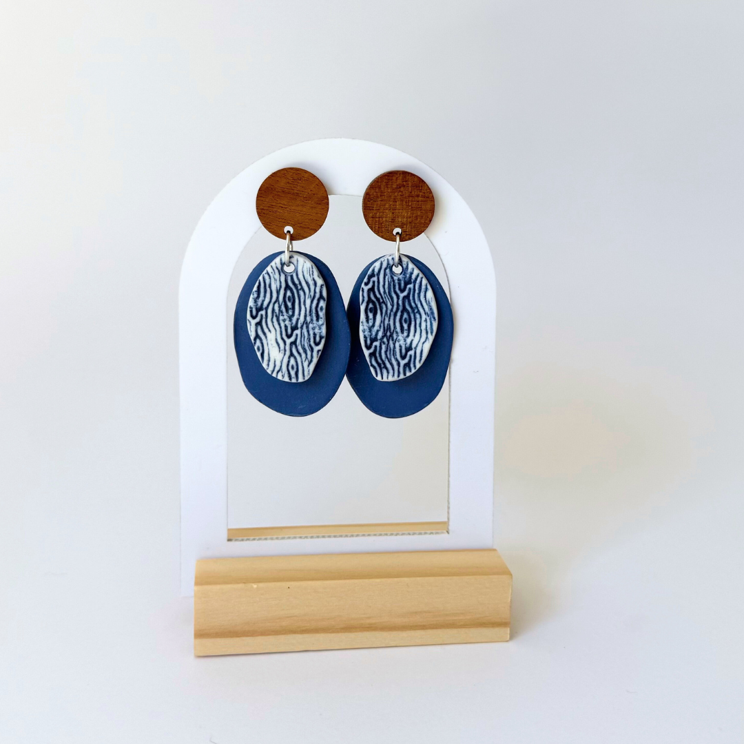 Handcrafted blue dangle earrings inspired by coastal textures. Featuring wooden studs and layered porcelain in deep ocean tones. By Fields and Seas.