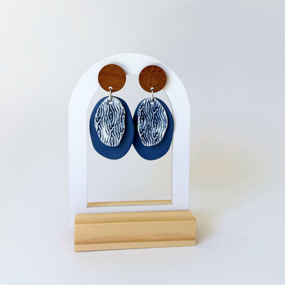 Handcrafted blue dangle earrings inspired by coastal textures. Featuring wooden studs and layered porcelain in deep ocean tones. By Fields and Seas.