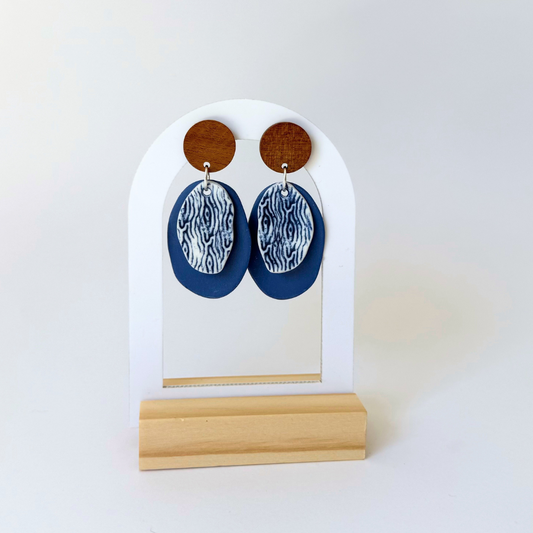 Handcrafted blue dangle earrings inspired by coastal textures. Featuring wooden studs and layered porcelain in deep ocean tones. By Fields and Seas.