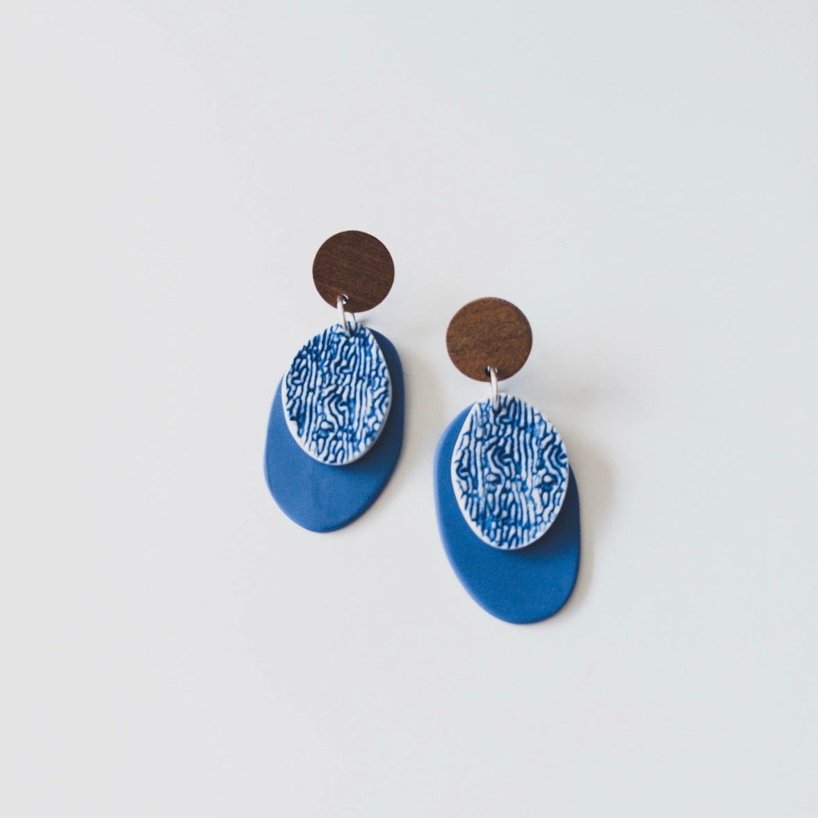Blue layered dangle earrings with wooden stud top, white textured porcelain oval and matte cobalt blue drop by Fields and Seas.