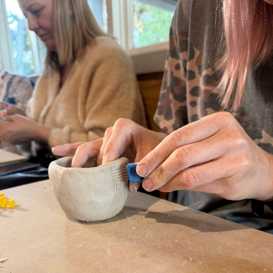 Person working on a ceramic bowl with another person in the background.