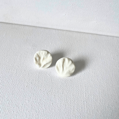 A pair of white porcelain coral-textured stud earrings displayed on a smooth piece of organic wood