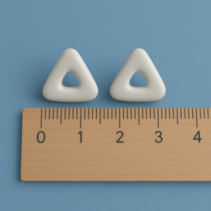 Two white triangular ceramic stud earrings with a wooden ruler for scale on a blue background