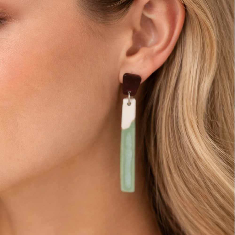 Close-up of a woman wearing a green/blue seafoam long dangle porcelain earring.