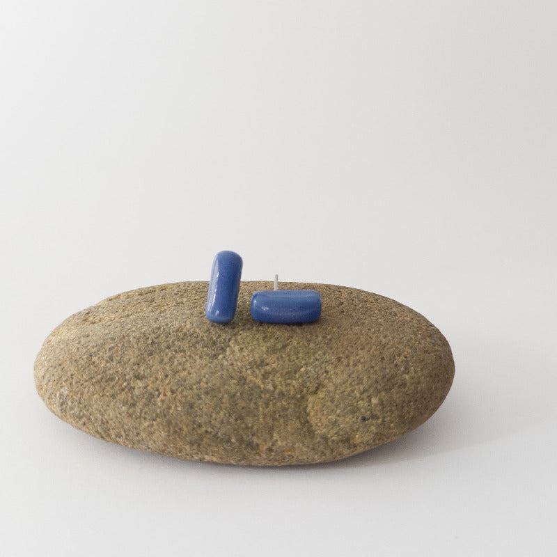 Blue porcelain bar stud earrings resting on a smooth stone