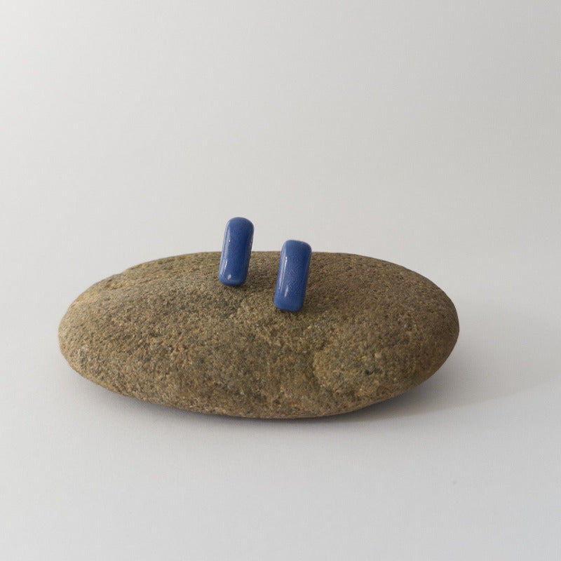 Blue porcelain bar stud earrings resting on a smooth stone