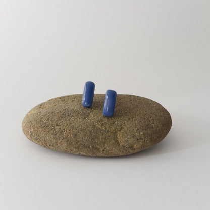 Blue porcelain bar stud earrings resting on a smooth stone