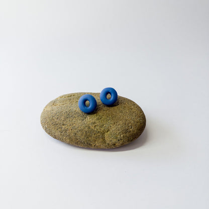 Cobalt blue porcelain circle stud earrings with oval cut center displayed on beach stone