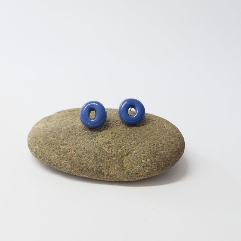 Blue porcelain circle studs resting on a beach stone with natural texture