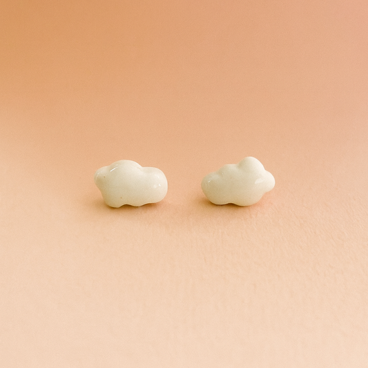 Close-up of handmade white porcelain cloud stud earrings on a neutral background
