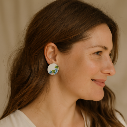Round hand-painted porcelain earrings with pink, blue, and yellow floral designs on a model.